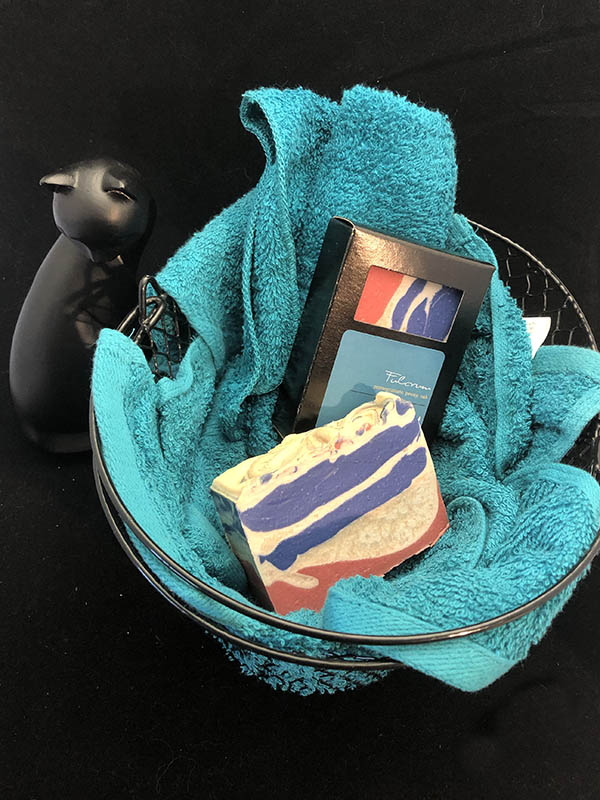 fulcrum soap bars, one in box one out, nested in a basket of teal towels with a sassy cat looking up at the viewer